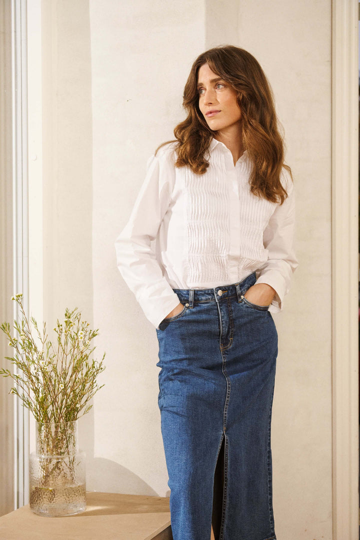 Jupe Dillin en denim, coupe midi avec fente frontale, portée avec chemise blanche, style urbain chic et décontracté.