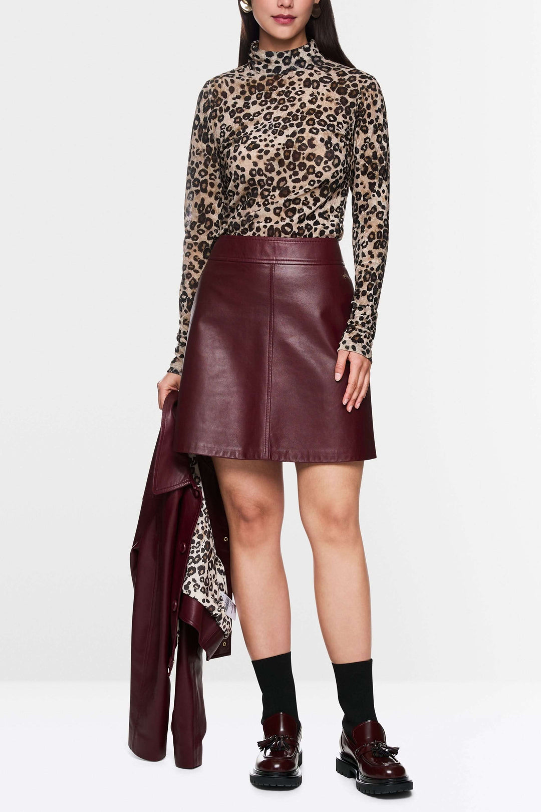 Femme portant une jupe en cuir marron avec coupe trapèze et col roulé léopard, style moderne et chic, jupe en cuir tendance.