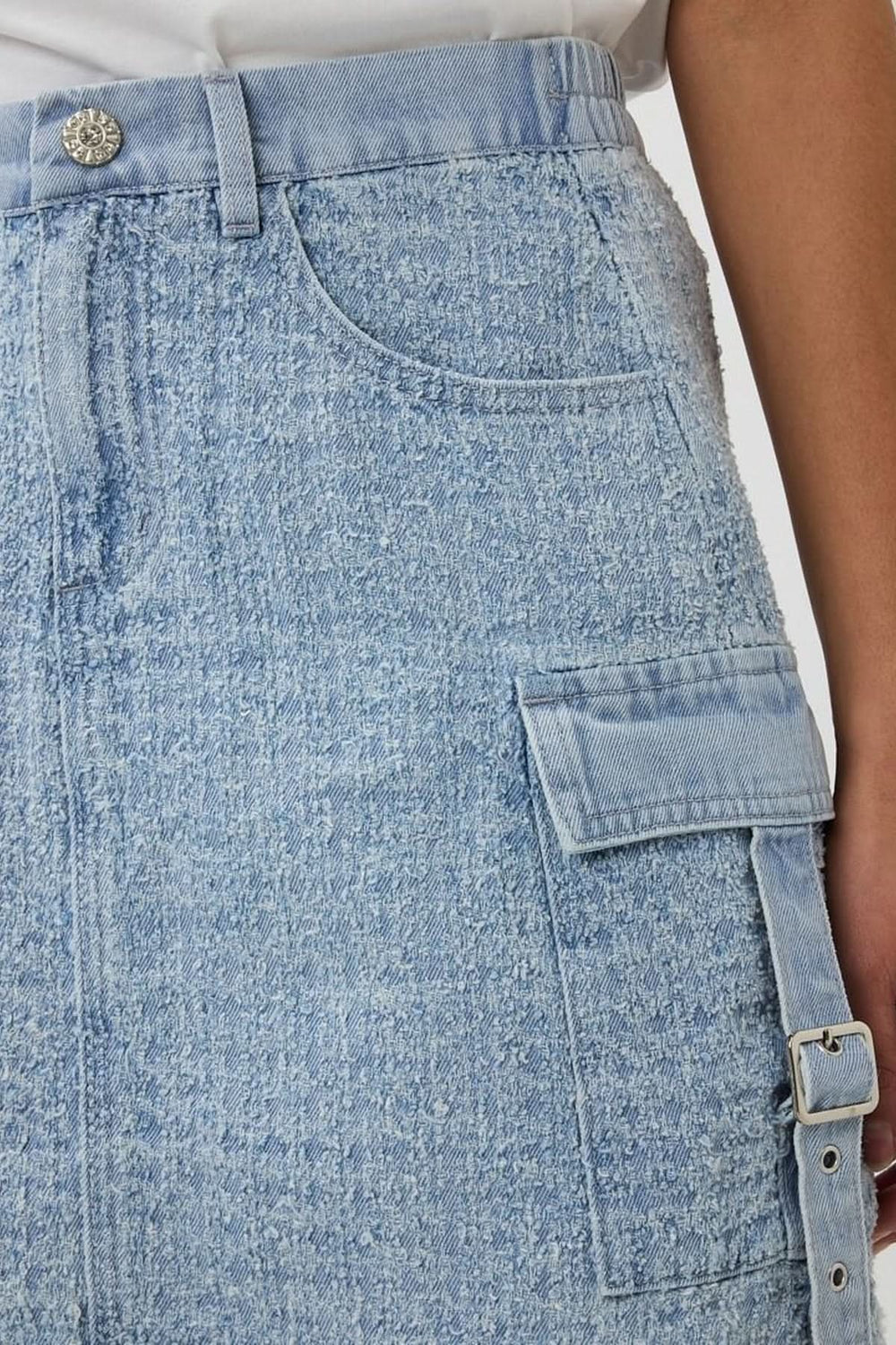 Détail d'une jupe en denim texturé, coupe trapèze avec poche cargo et sangle ajustable.
