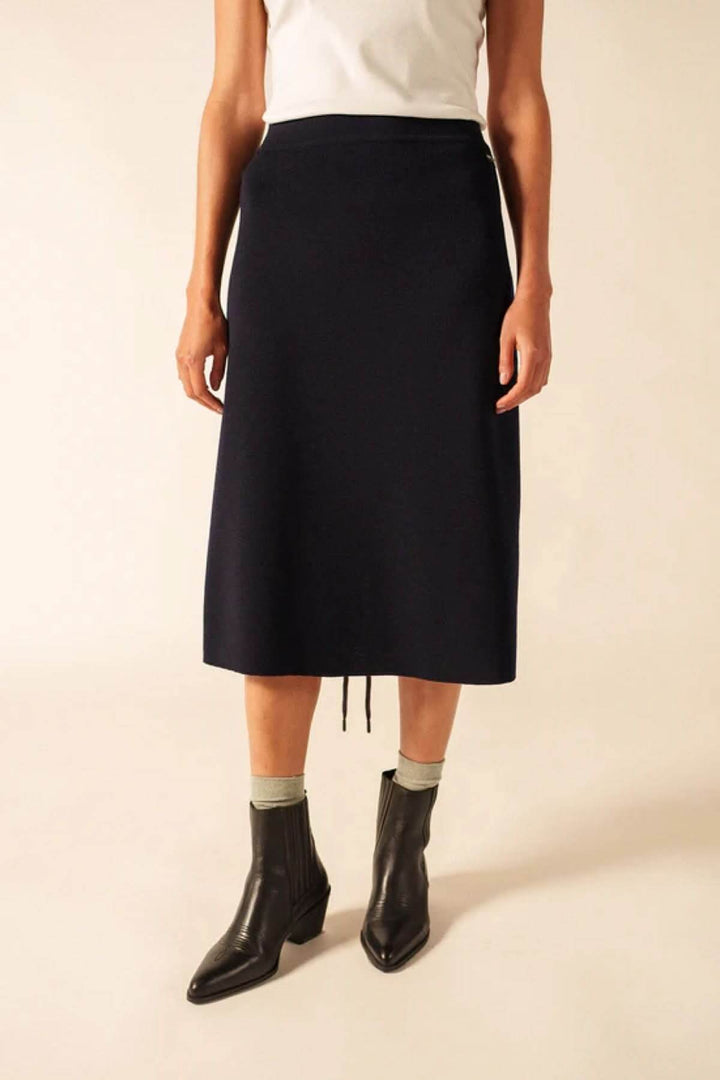 Jupe midi en laine noire avec coupe fluide et taille élastique, portée avec des bottines noires.