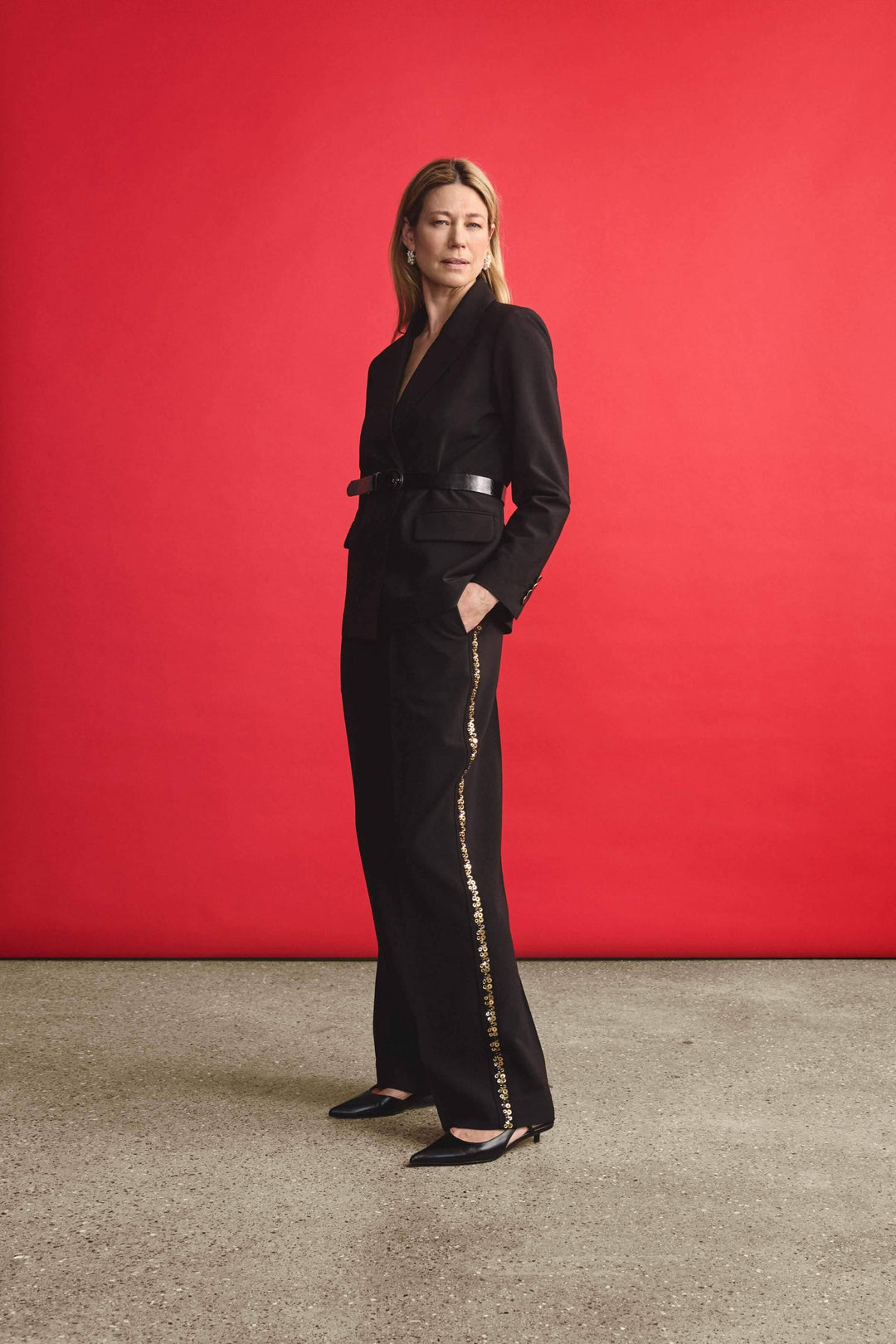 Femme en pantalon noir large avec bande dorée, look élégant sur fond rouge.