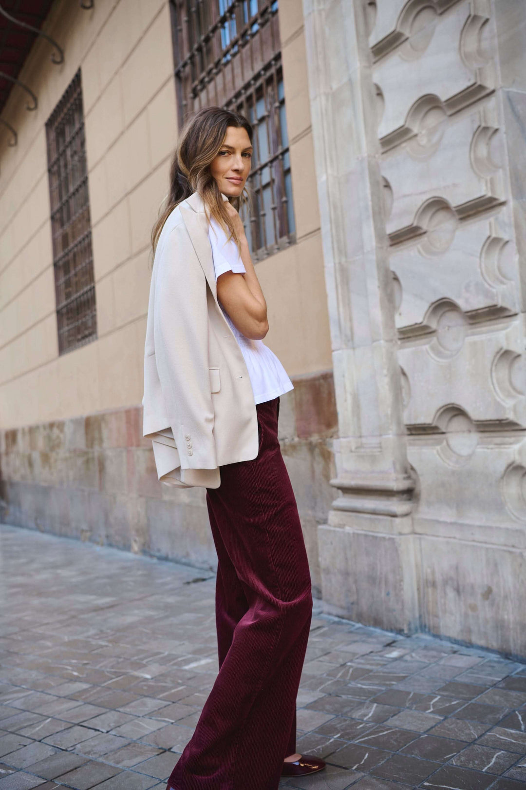 Femme portant le Pantalon Clarissi en velours côtelé avec un blazer crème, style rétro-chic élégant et moderne en extérieur.