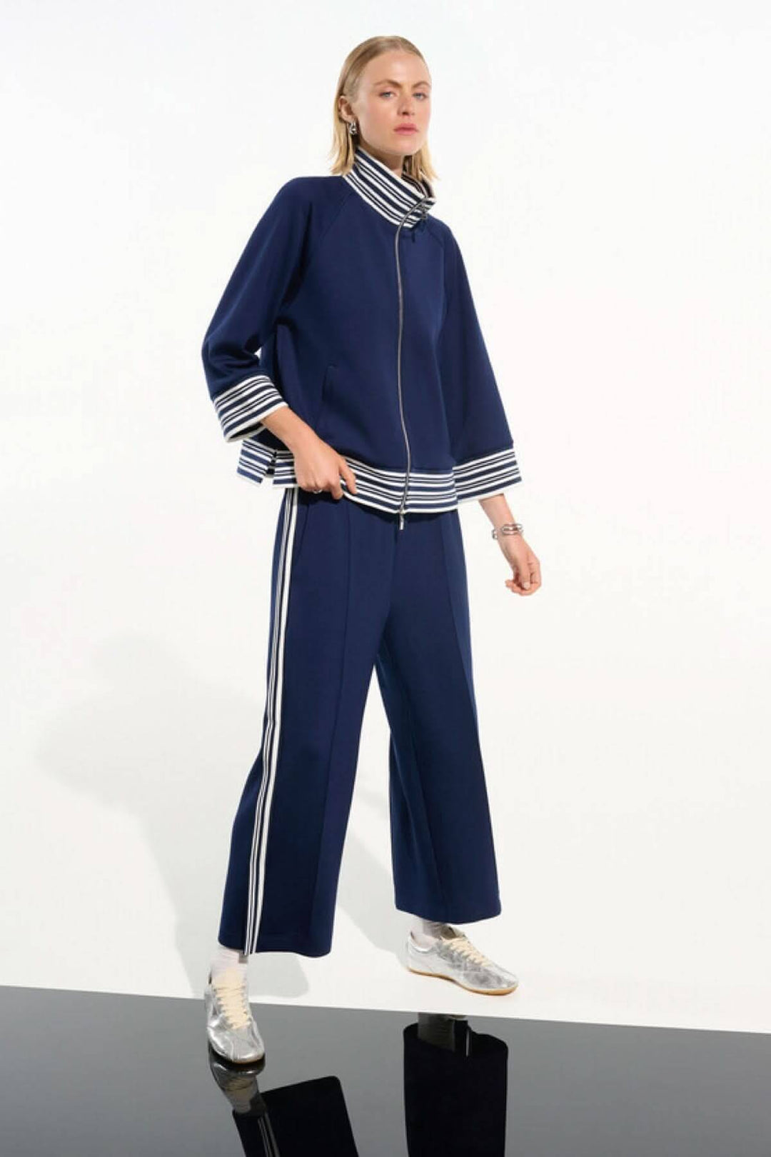 Femme portant un pantalon athlétique à bandes contrastantes bleu avec une veste assortie, posant dans un style décontracté et moderne.