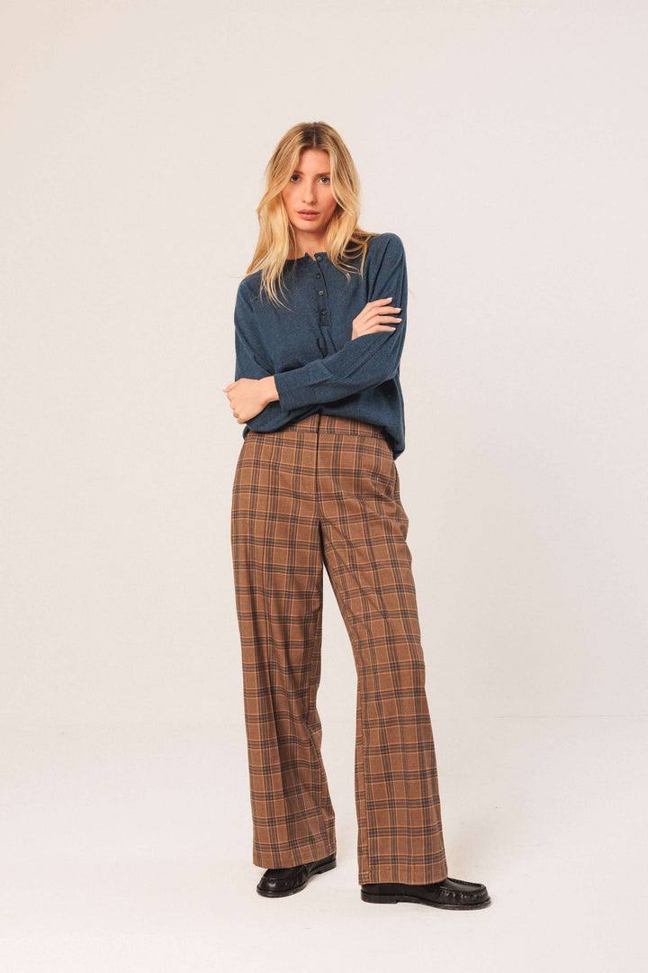 Femme portant un pantalon à carreaux large et fluide, taille haute, avec une chemise unie, style chic et moderne.
