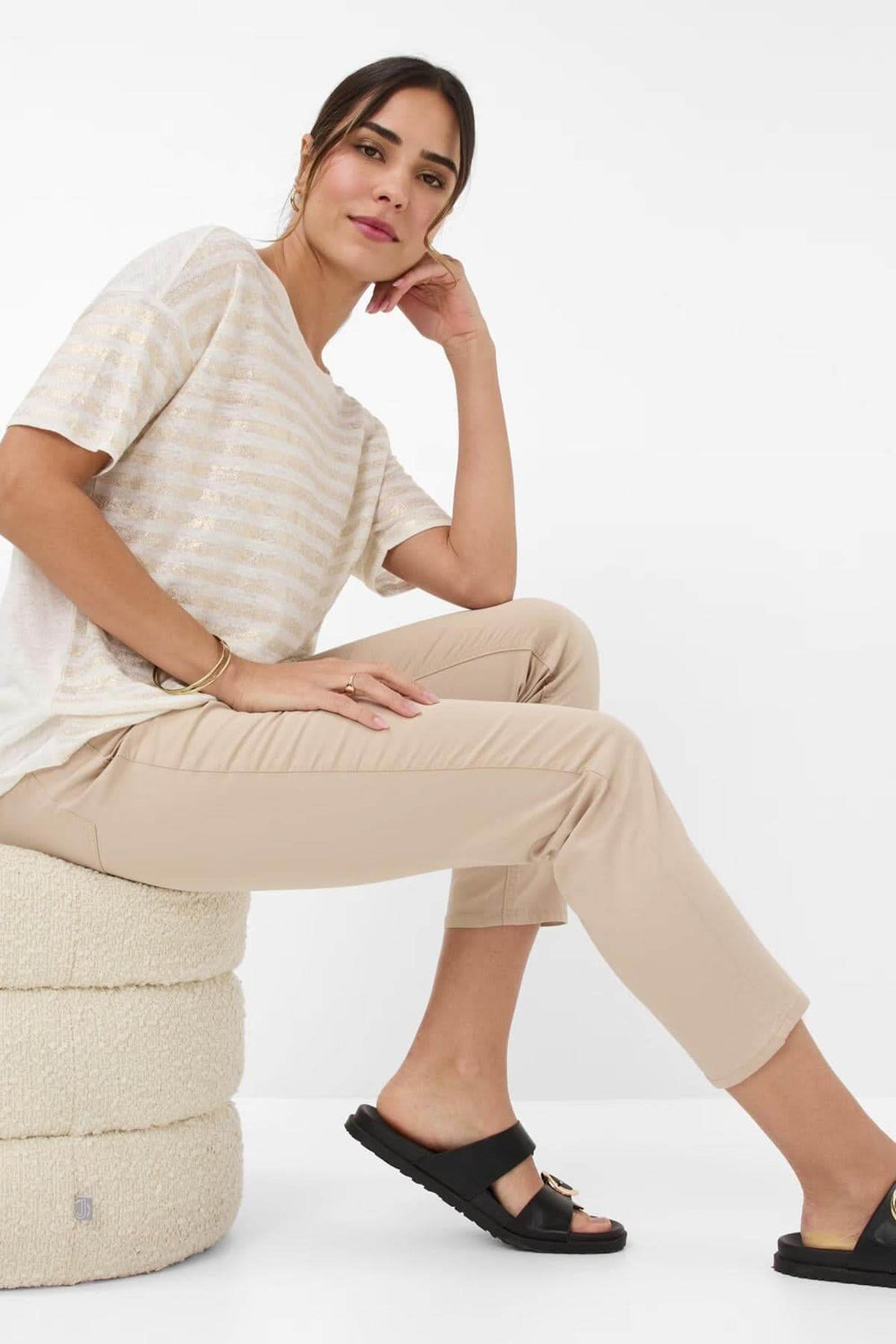 Femme portant un pantalon chino MARY S ultra léger, avec un pull léger et des sandales noires sur un pouf.