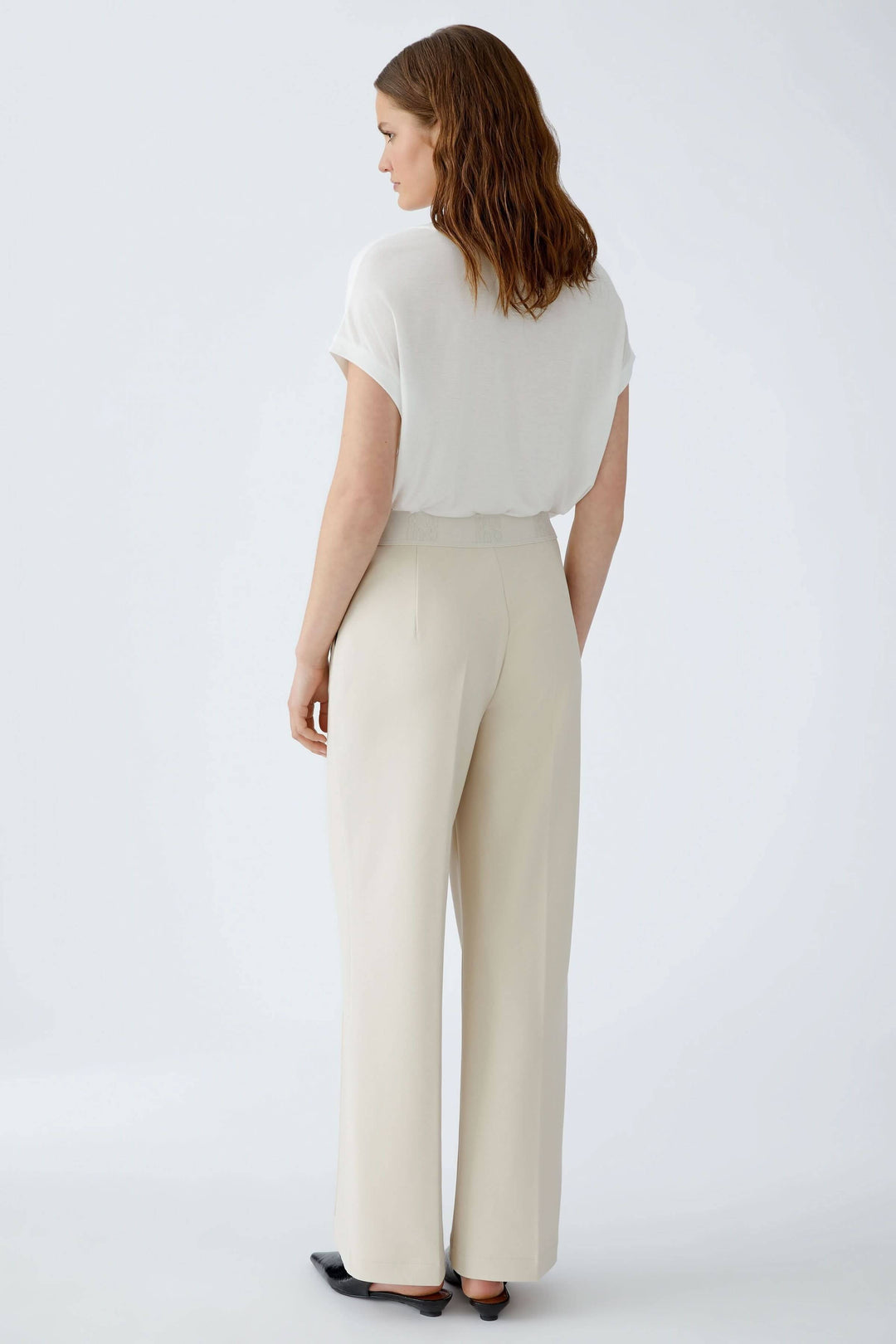 Femme portant un pantalon droit à taille élastique logo, coupe élégante avec plis marqués et poches latérales. Mode quotidienne soignée.