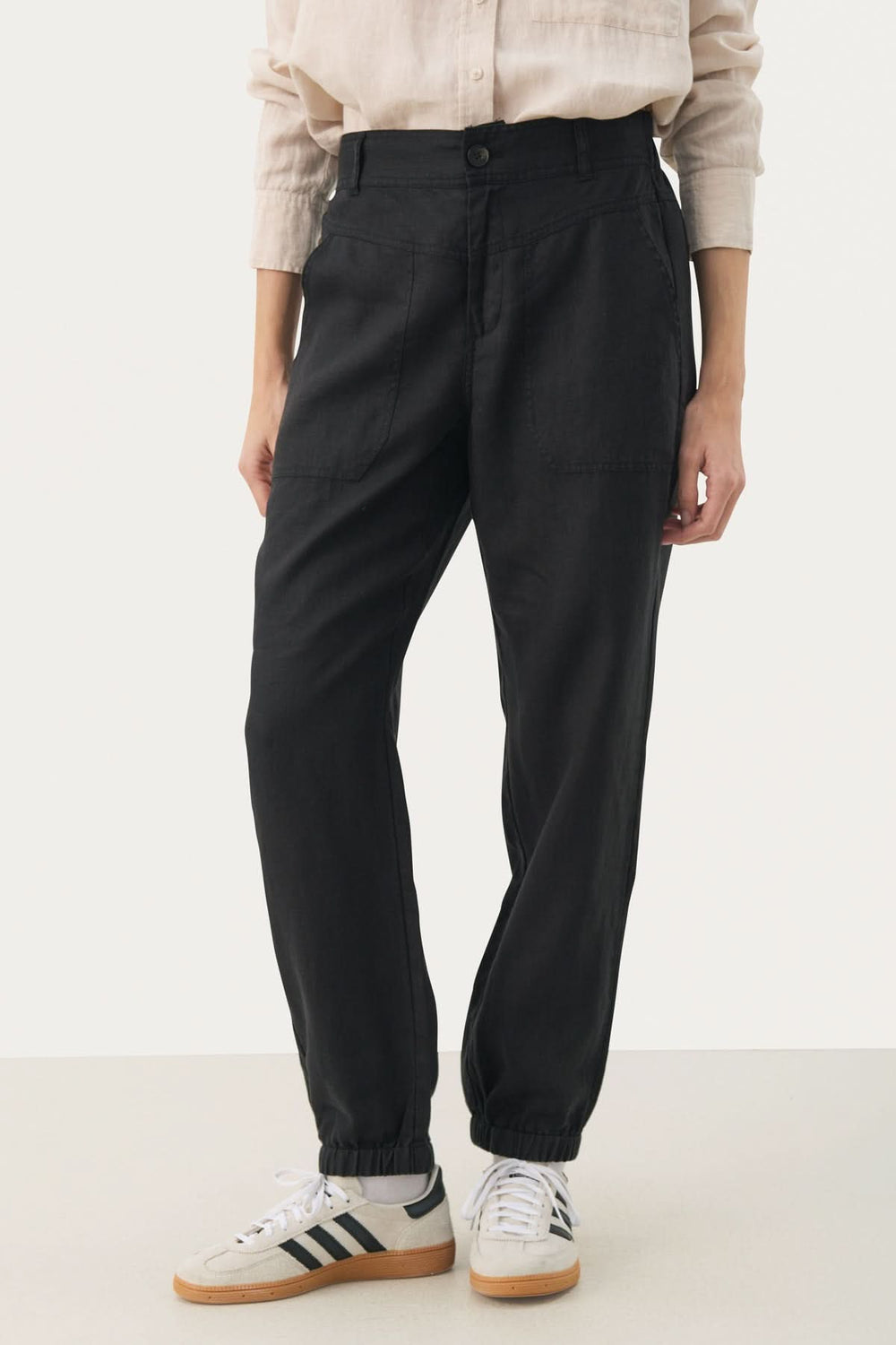 Pantalon en lin Shenas noir, coupe ample avec poches avant et chevilles élastiques, porté avec des sneakers.