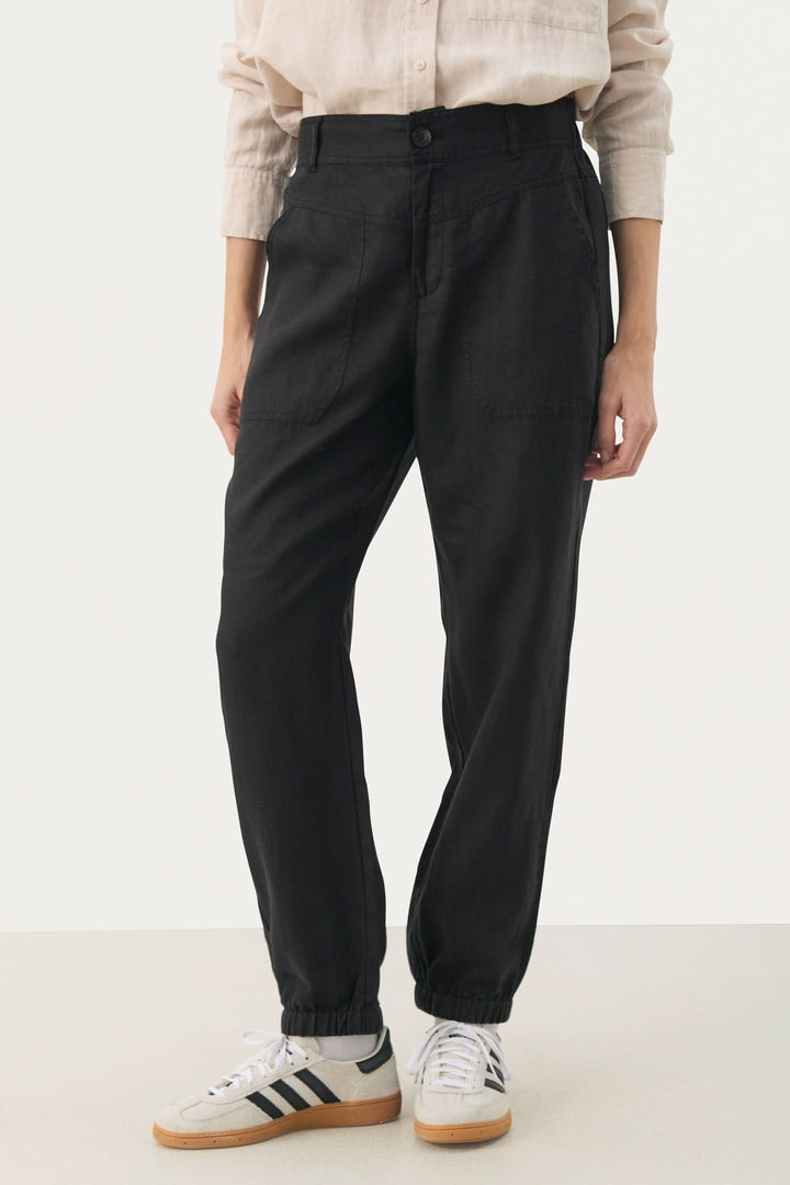 Pantalon en lin Shenas noir, coupe ample avec poches avant et chevilles élastiques, porté avec des sneakers.