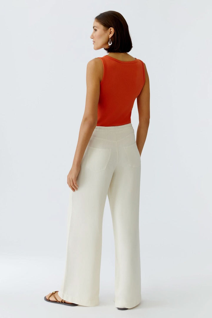 Femme portant un pantalon fluide à cordon de serrage beige, vu de dos, coupe large, style décontracté et élégant, avec top rouge sans manches.