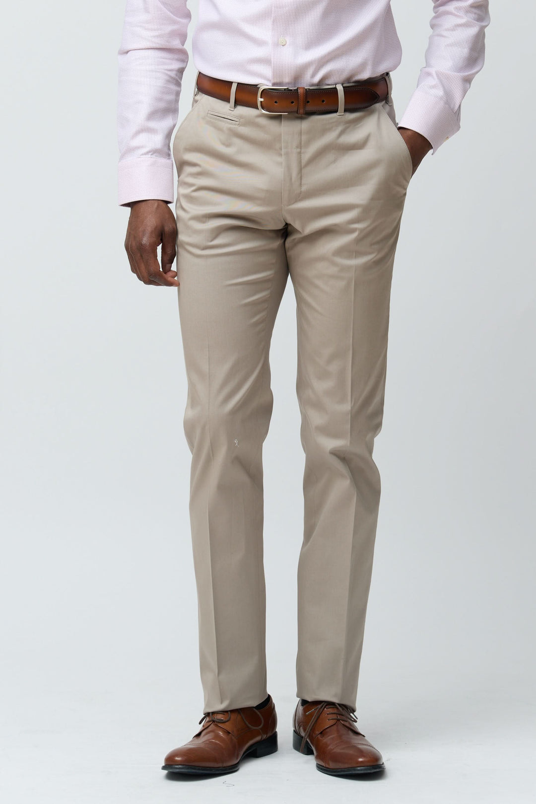 Homme portant un pantalon habillé coupe ajustée beige avec ceinture marron et chaussures élégantes.