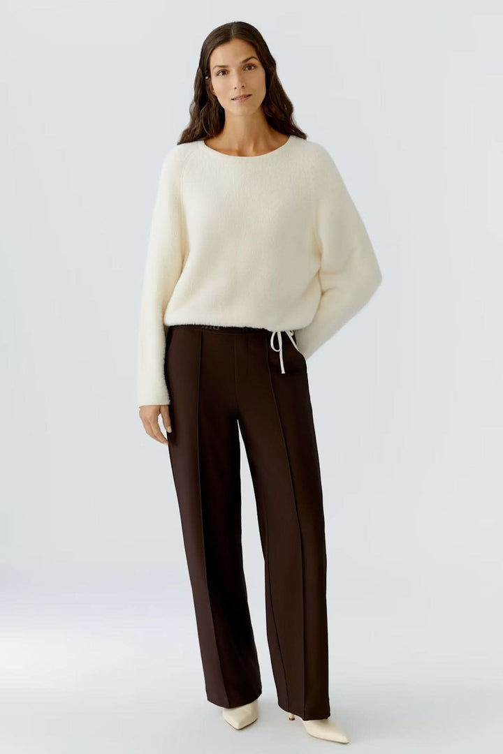 Femme portant un pantalon à jambe large en jersey technique avec ceinture élastique, associé à un pull blanc et des mules pointues.