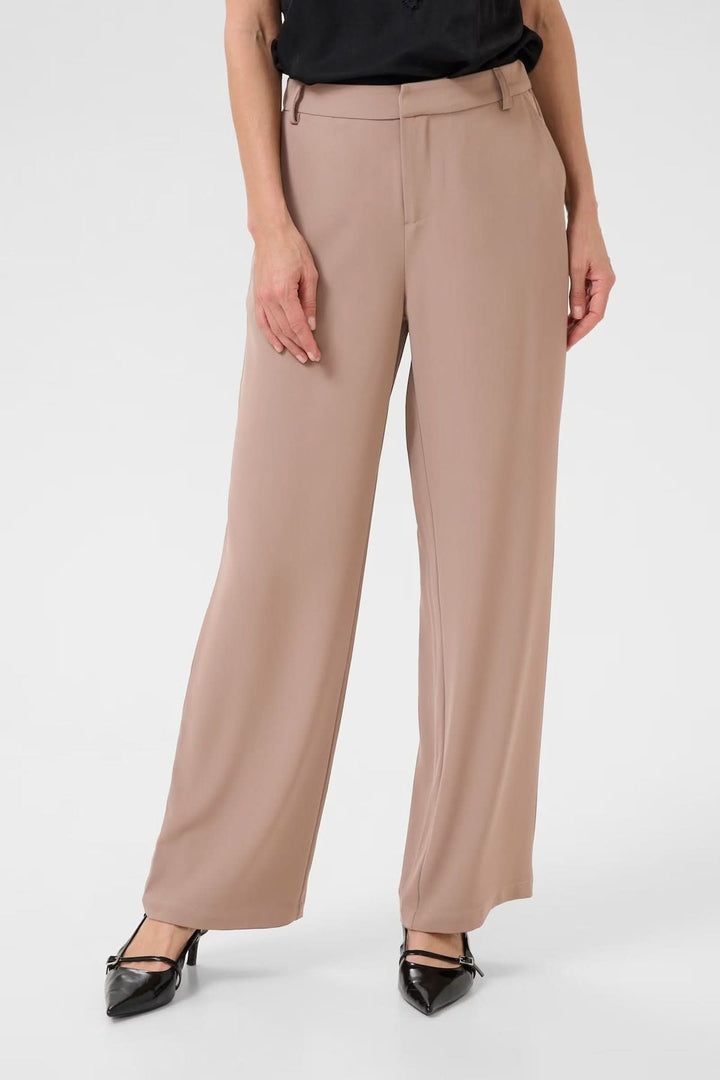 Femme portant un pantalon à jambe large beige avec taille régulière et passants de ceinture, idéal pour un style professionnel.