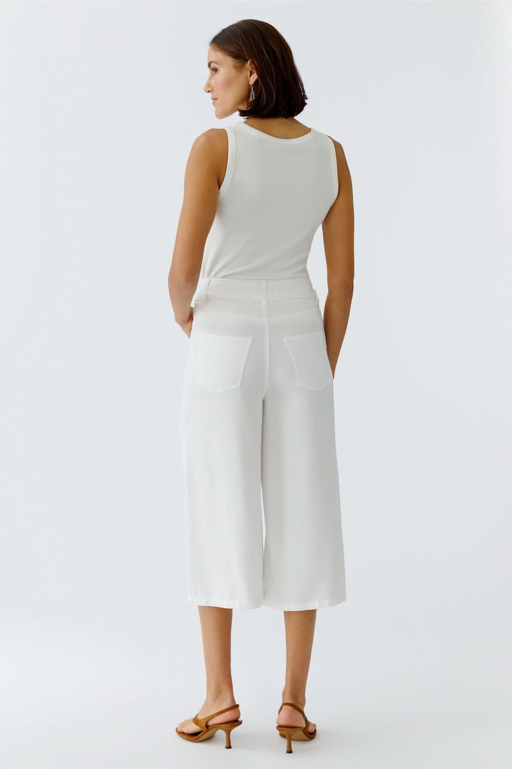 Femme portant un pantalon trois quarts à taille nouée blanc, coupe fluide, vue de dos, parfait pour l'été.