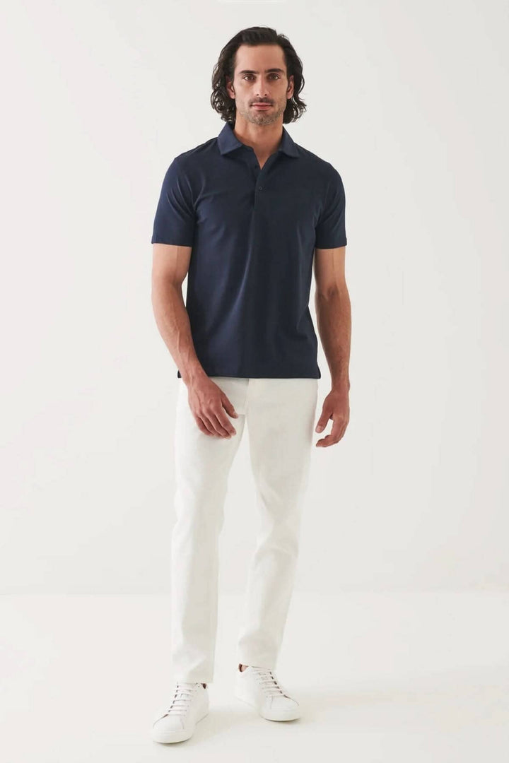 Polo à manches courtes bleu marine, coupe fluide, confort optimal, habillé avec un pantalon blanc.