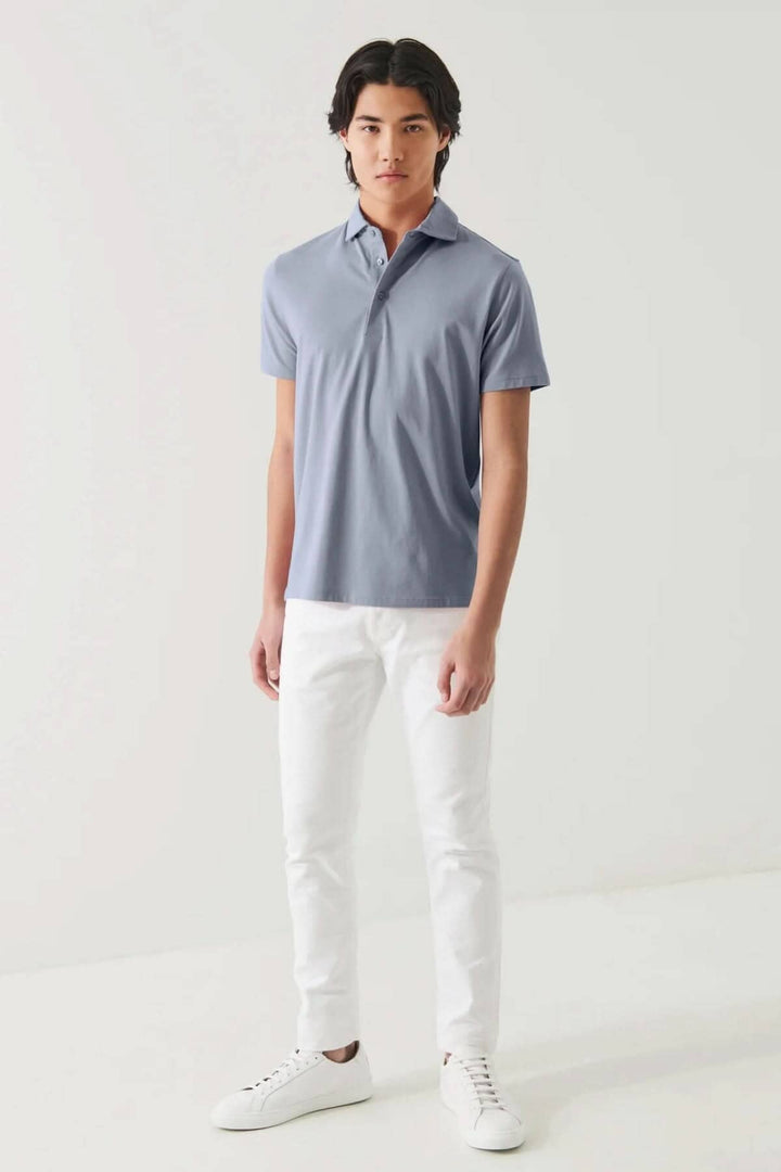 Homme en polo manches courtes bleu, tenue chic et décontractée avec pantalon blanc.