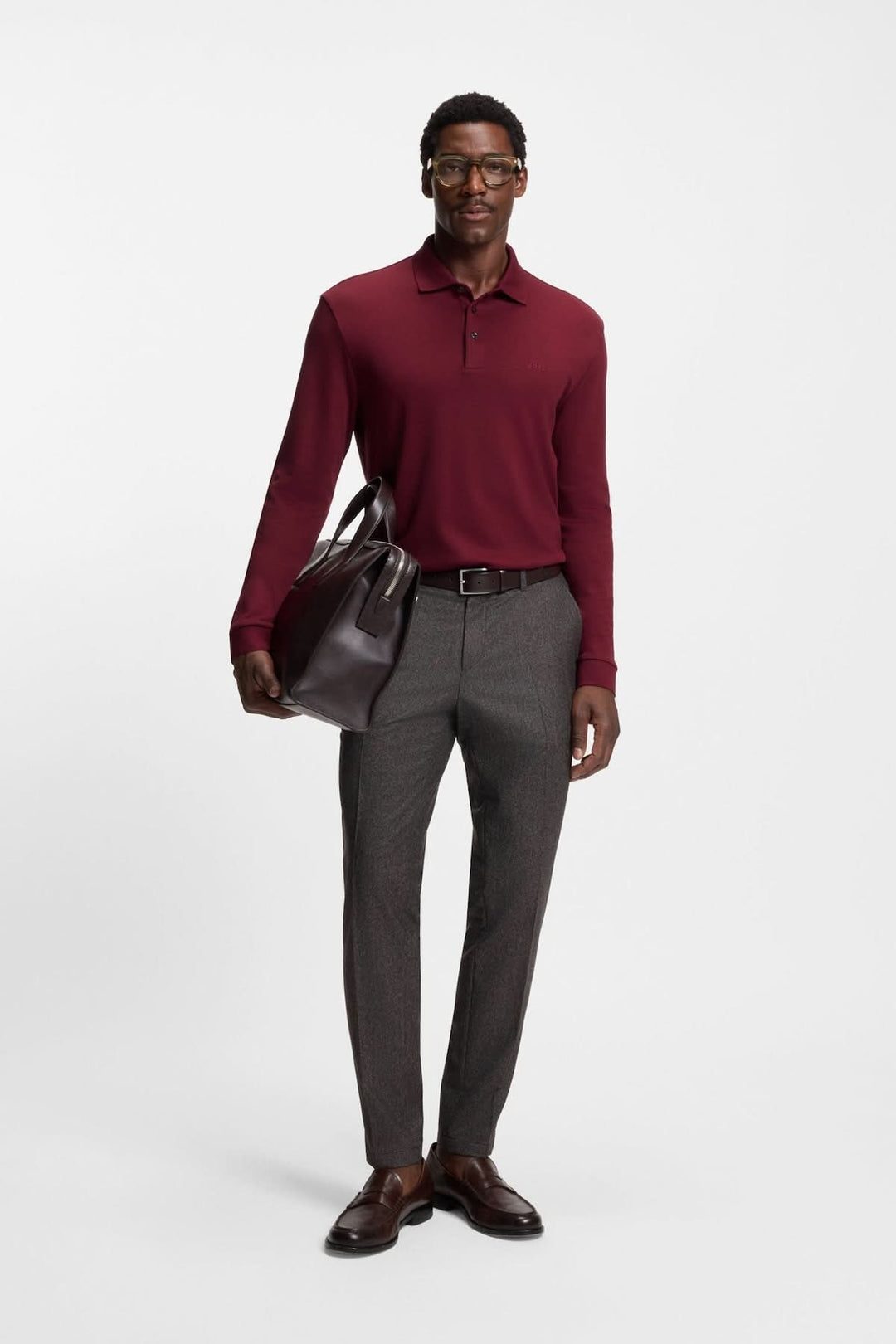 Homme portant un Polo manches longues Pado bordeaux avec un pantalon gris et un sac en cuir, représentant l'élégance décontractée de BOSS.