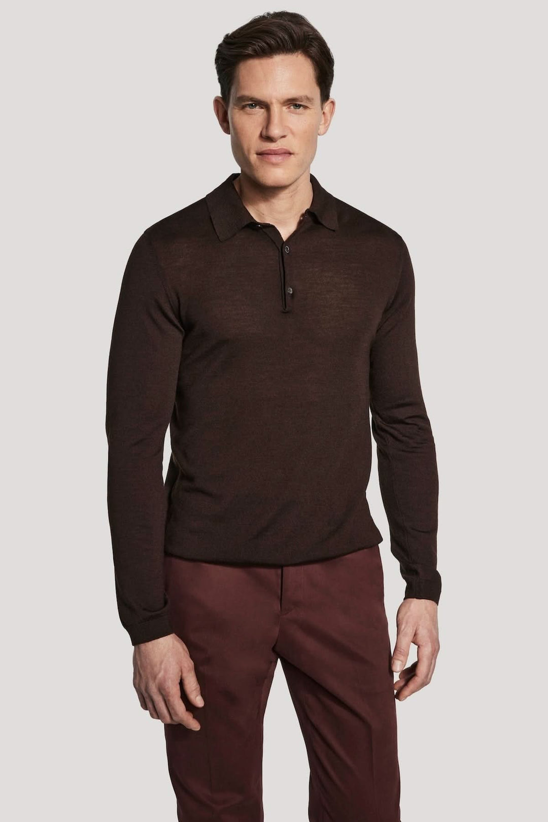 Homme portant un polo manches longues en laine mérinos et soie, élégant et moderne, couleur sombre, sur fond clair.