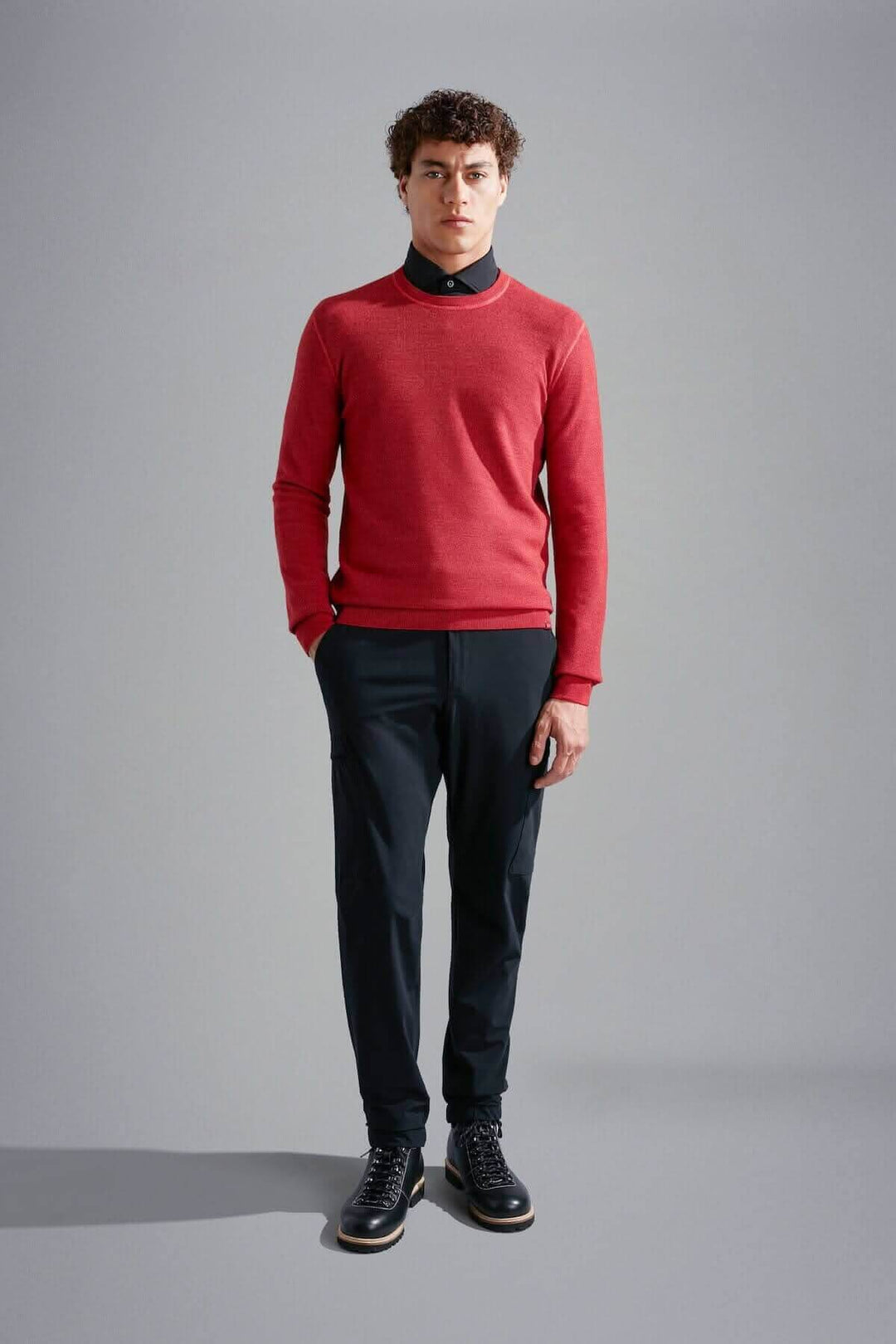 Homme portant un pull en laine mérinos rouge avec une chemise noire et un pantalon noir.