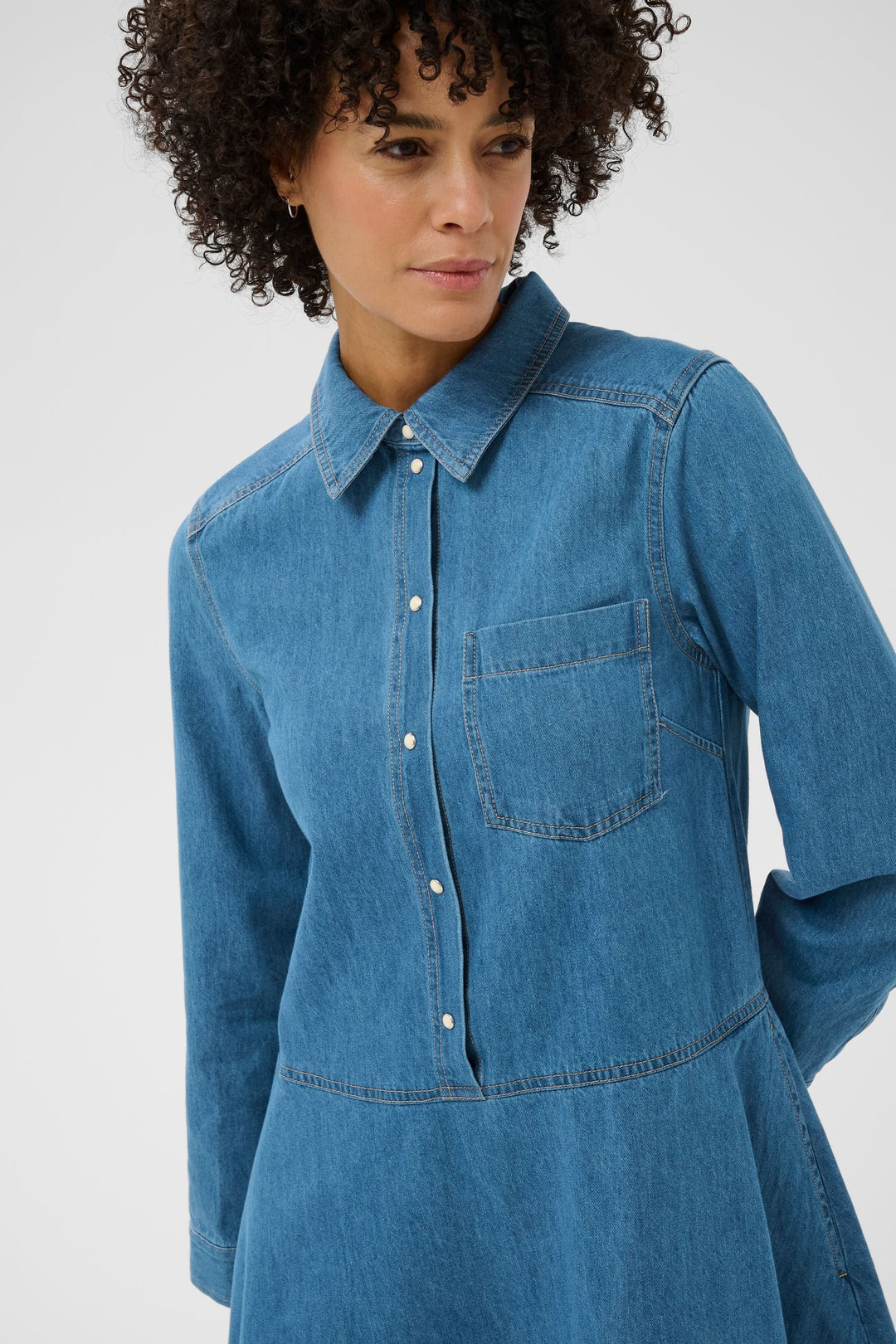 Femme portant la Robe chemise Augustine en denim, coupe évasée et col structuré, avec manches longues et poche poitrine.
