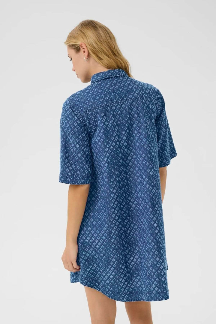 Femme portant une robe-chemise en denim léger avec motifs géométriques, vue de dos, manches courtes et col classique.