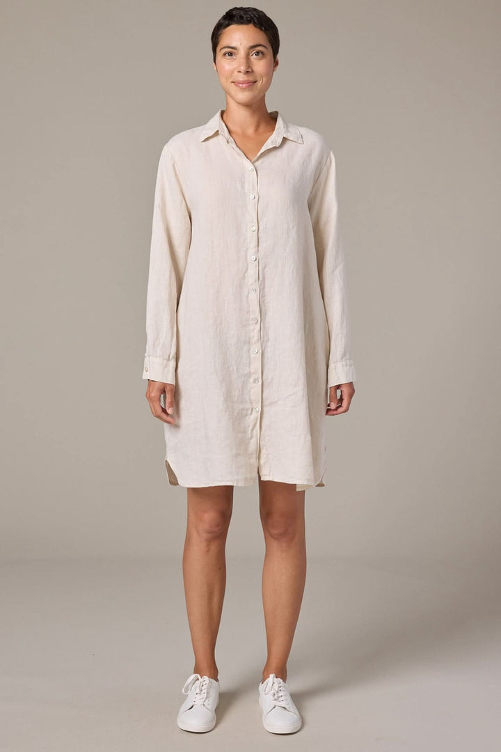 Femme portant une robe chemise en lin à manches longues, coupe droite et fluide, avec fermeture boutonnée et col classique.