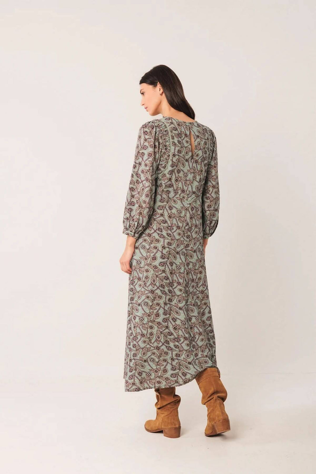 Femme portant une robe longue au motif géométrique avec manches bouffantes et bottes en daim, vue de dos.