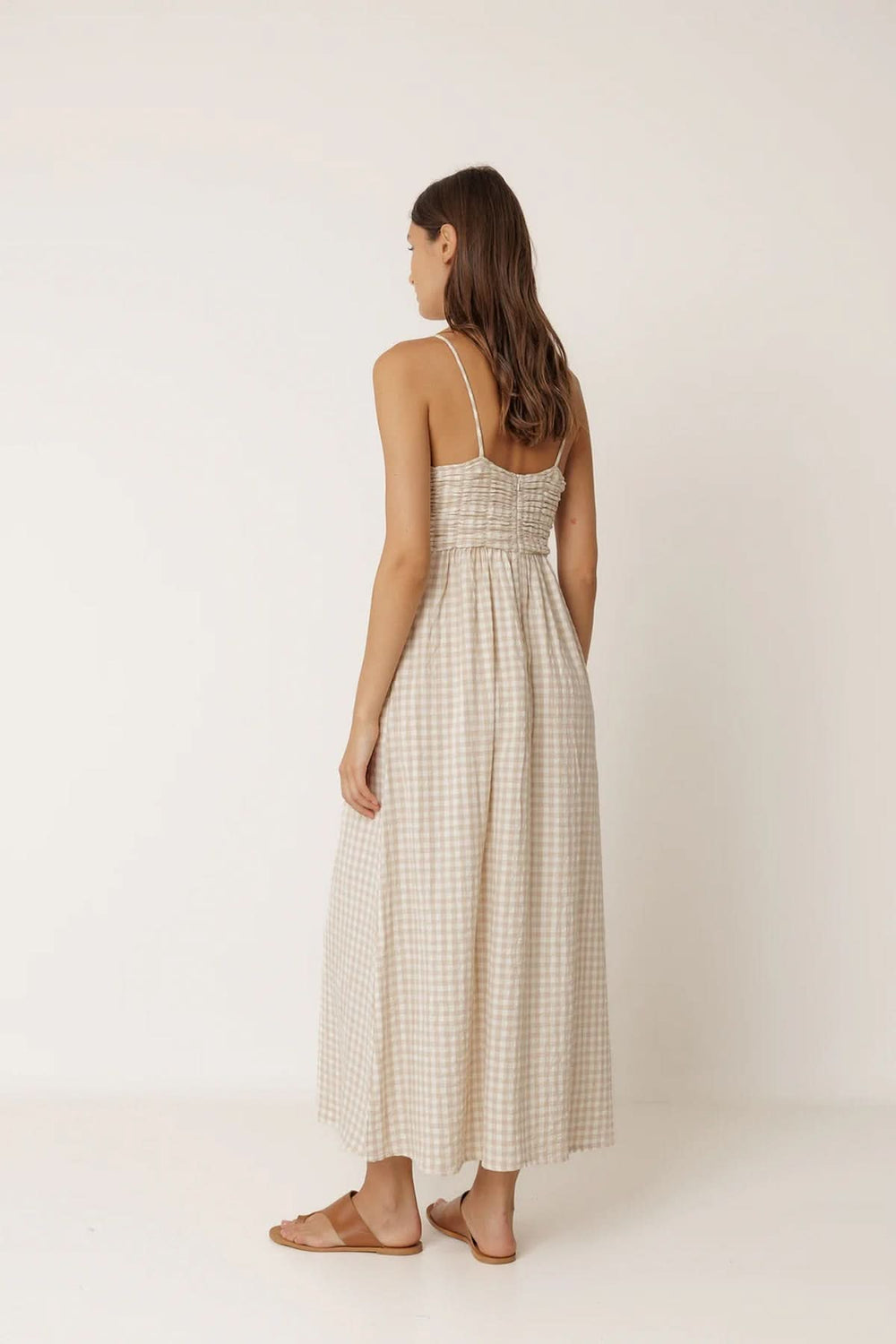 Vue de dos d'une femme portant une robe midi à motif vichy avec fines bretelles, élégance naturelle et confort estival.