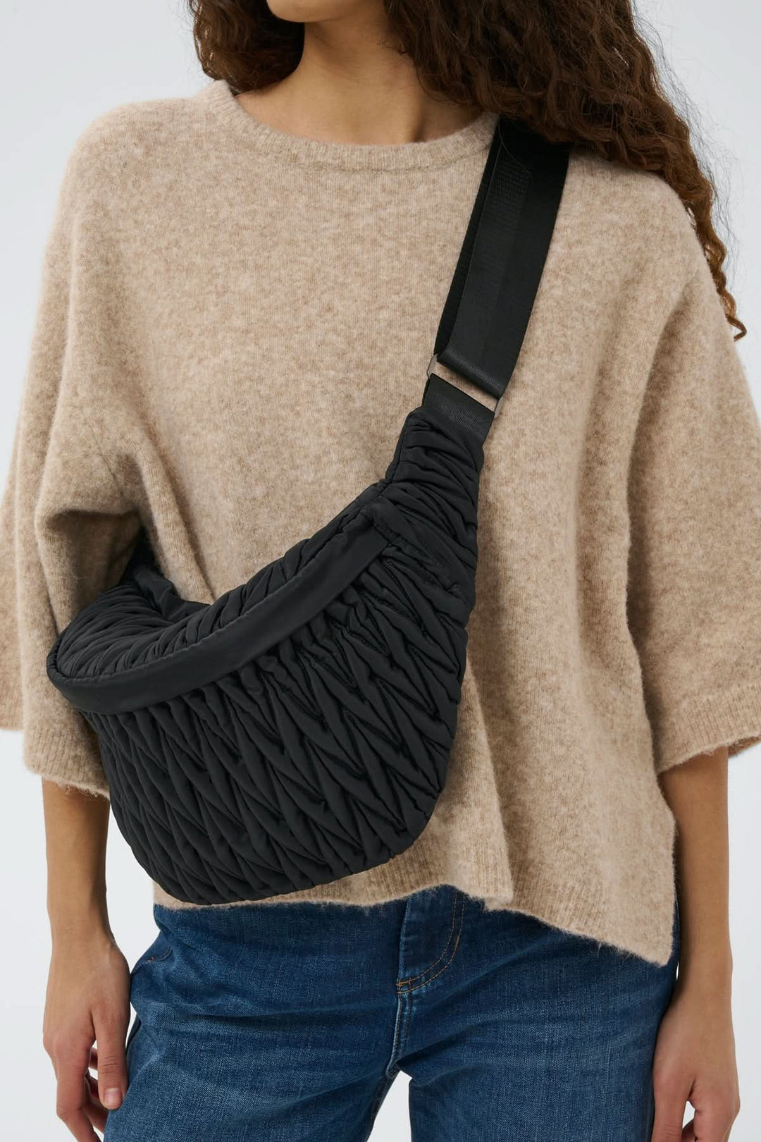 Femme portant un Sac bandoulière matelassé Samy Bumbag noir avec finition froncée, tenue urbaine décontractée, bandoulière ajustable.