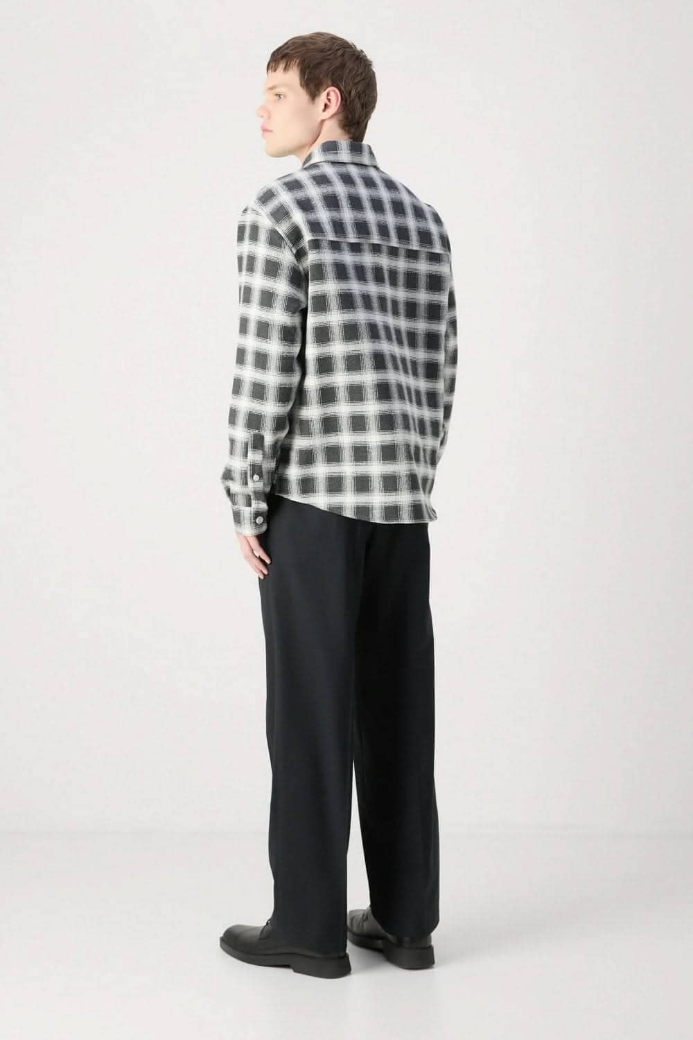Homme portant une surchemise en flanelle à carreaux noir et blanc, vue de dos, style superposé.