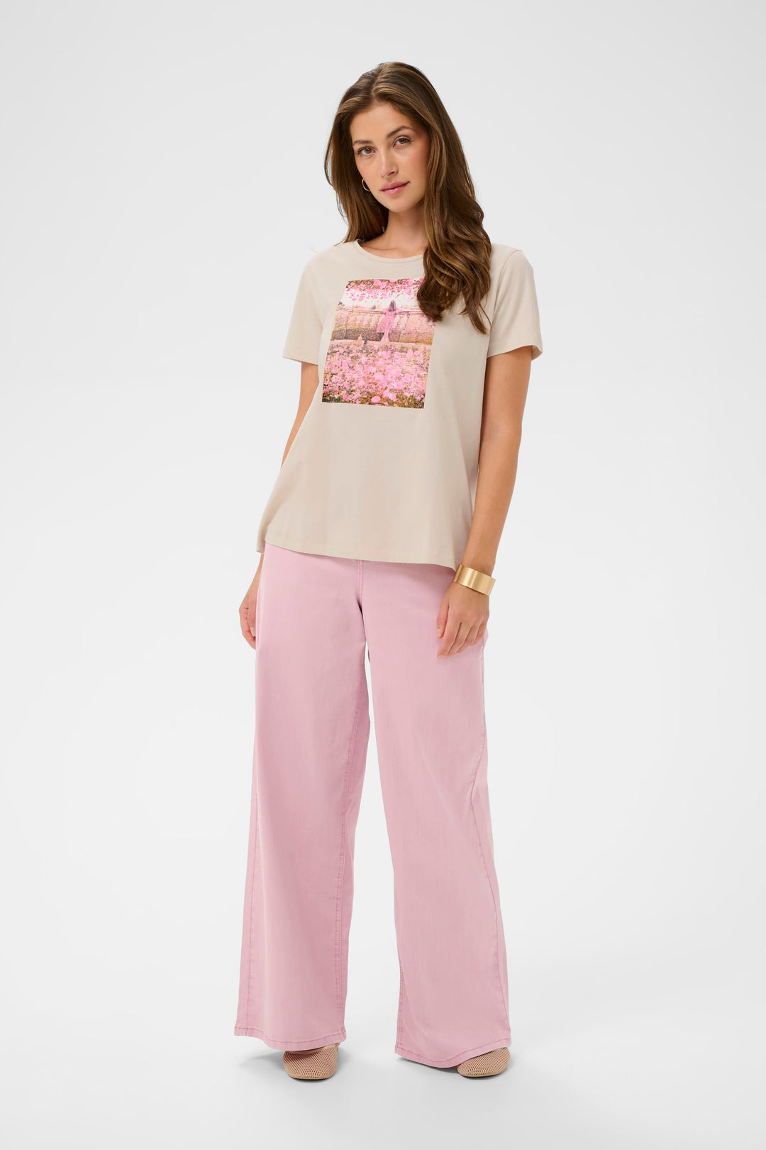 Femme portant un T-shirt Joliy à imprimé artistique, manches courtes et coupe droite, associé à un pantalon rose ample.