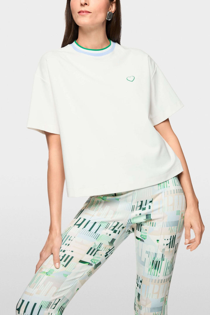 T-shirt avec détails en forme de cœur et à rayures, col contrastant, mannequin portant un pantalon imprimé, look moderne.