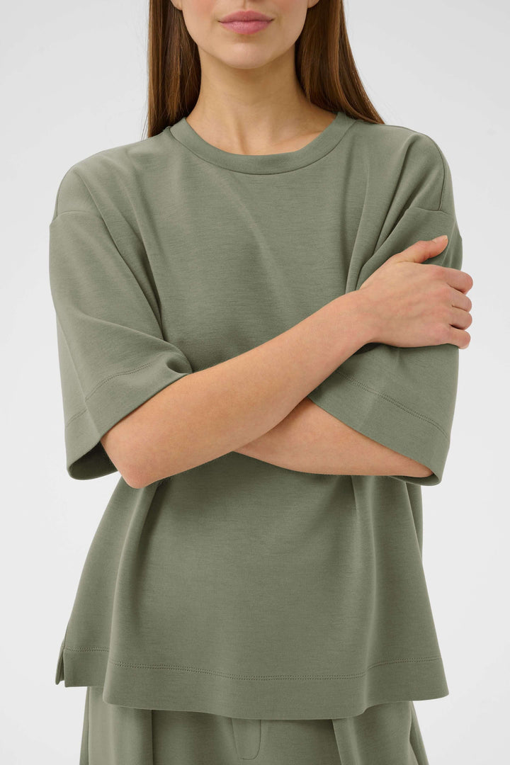 Femme portant un T-shirt coupe ample Pannie vert avec manches courtes, encolure ronde, style décontracté et moderne, matière fluide.