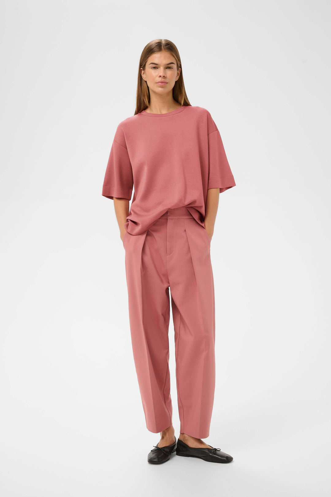 Femme portant un T-shirt coupe ample Pannie rose avec pantalon assorti, style décontracté moderne et épuré.