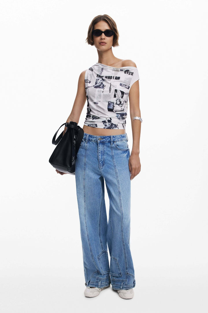 Femme portant un t-shirt drapé asymétrique avec imprimé typographique et un jean large, style moderne et urbain.