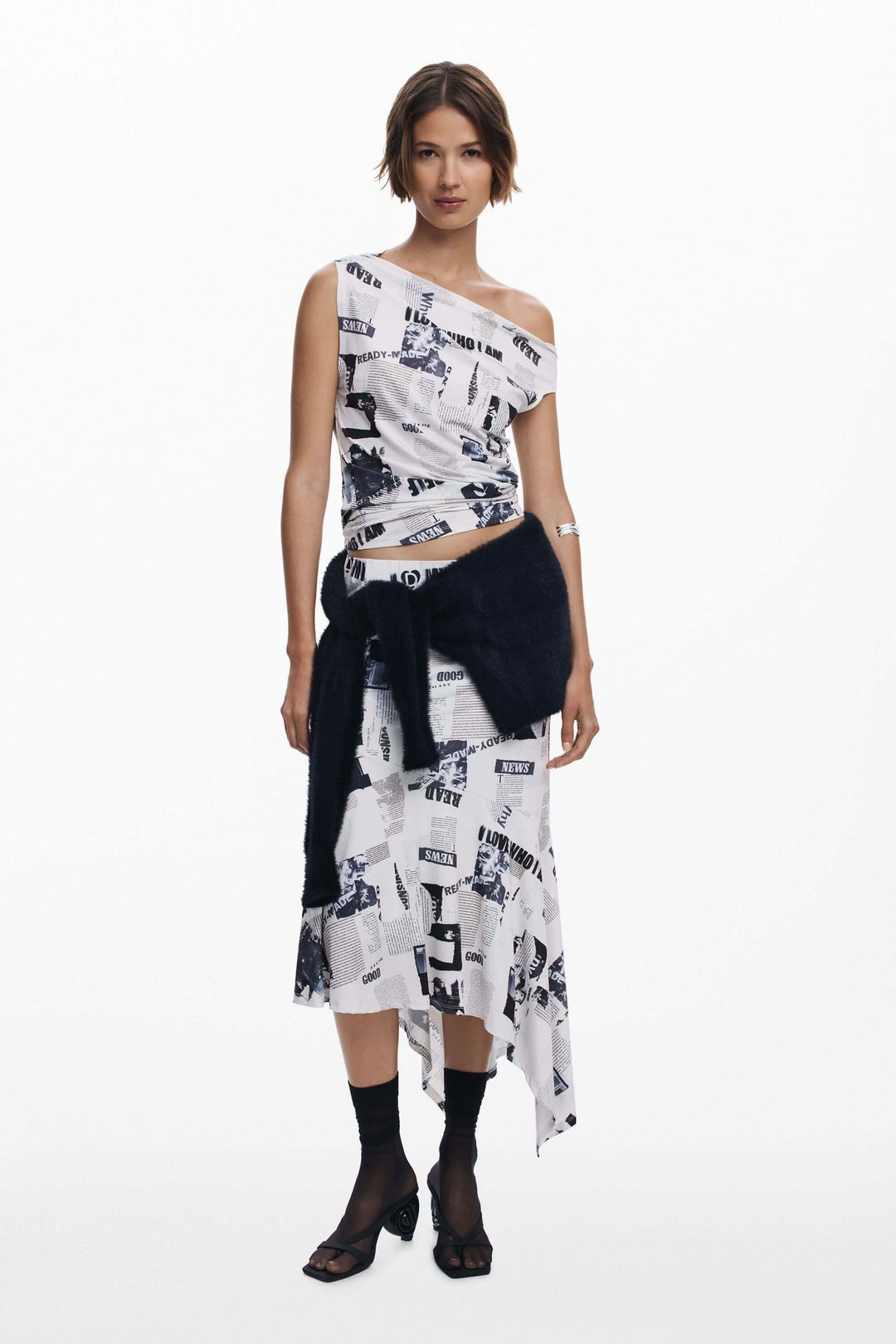 Femme portant un T-shirt drapé asymétrique à imprimé typographique, avec une jupe ou un pantalon taille haute, moderne et élégant.