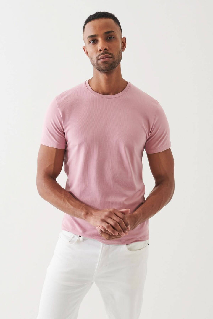 Homme portant un T-shirt en coton Pima rose, style décontracté avec un pantalon blanc, mettant en valeur le confort et l&
