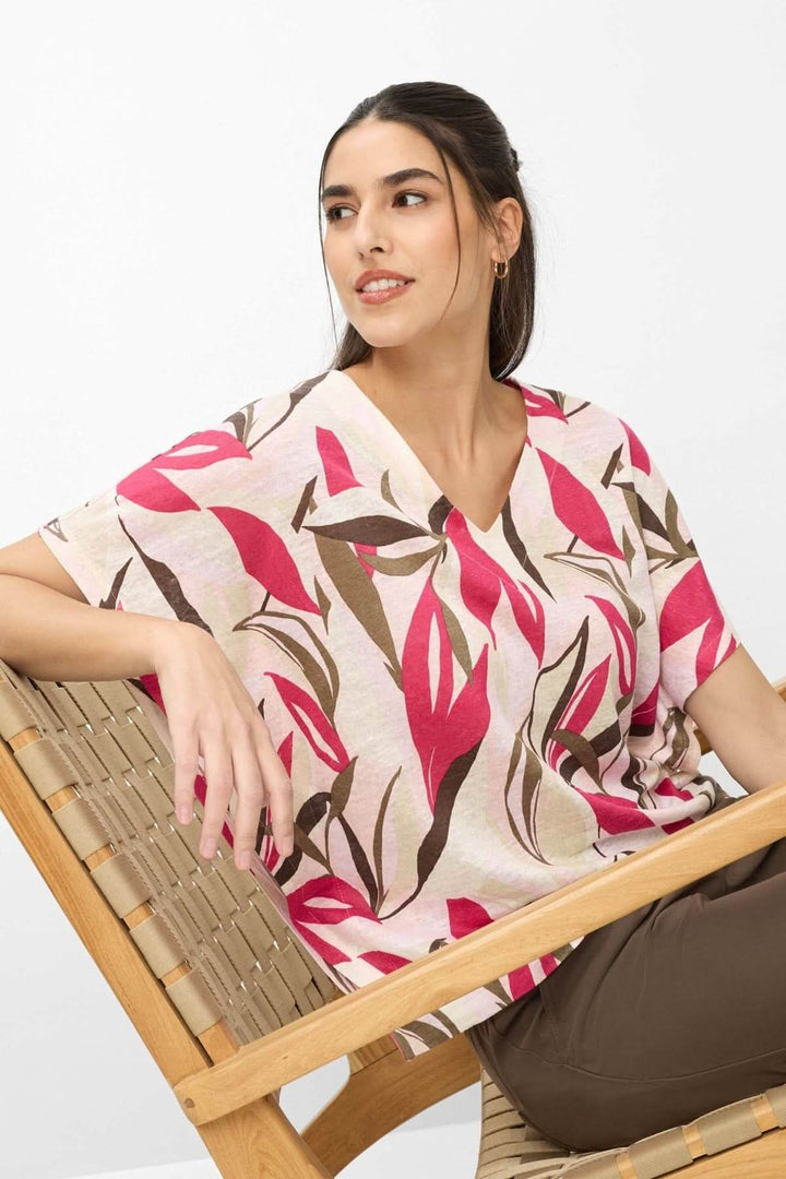 Femme portant le T-shirt imprimé végétal Cassie avec encolure en V et coupe ample dans une chaise en bois, style quotidien décontracté.