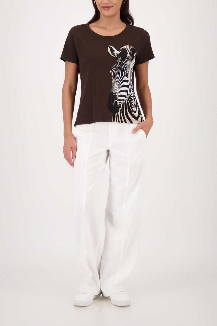 Femme portant un T-shirt imprimé zèbre avec une coupe simple et encolure arrondie, idéal pour un look moderne avec un pantalon blanc.