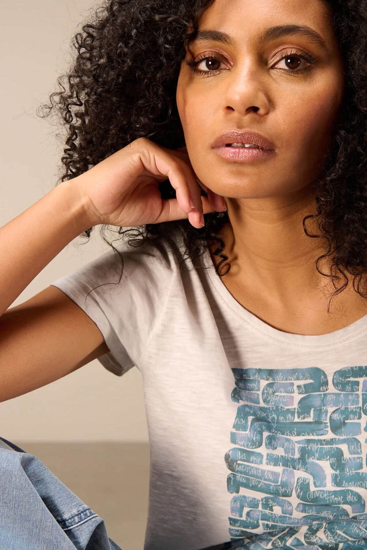 Femme portant un T-shirt à manches courtes coupe décontractée avec motif, assise dans un environnement décontracté.