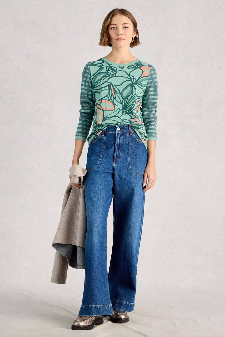 Femme portant un T-shirt à manches longues Clara avec un imprimé floral et pantalon en jean large, tenue décontractée.