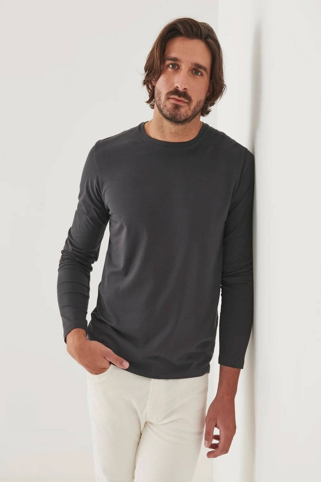 Homme portant un t-shirt à manches longues gris en coton Pima, contre un mur blanc.