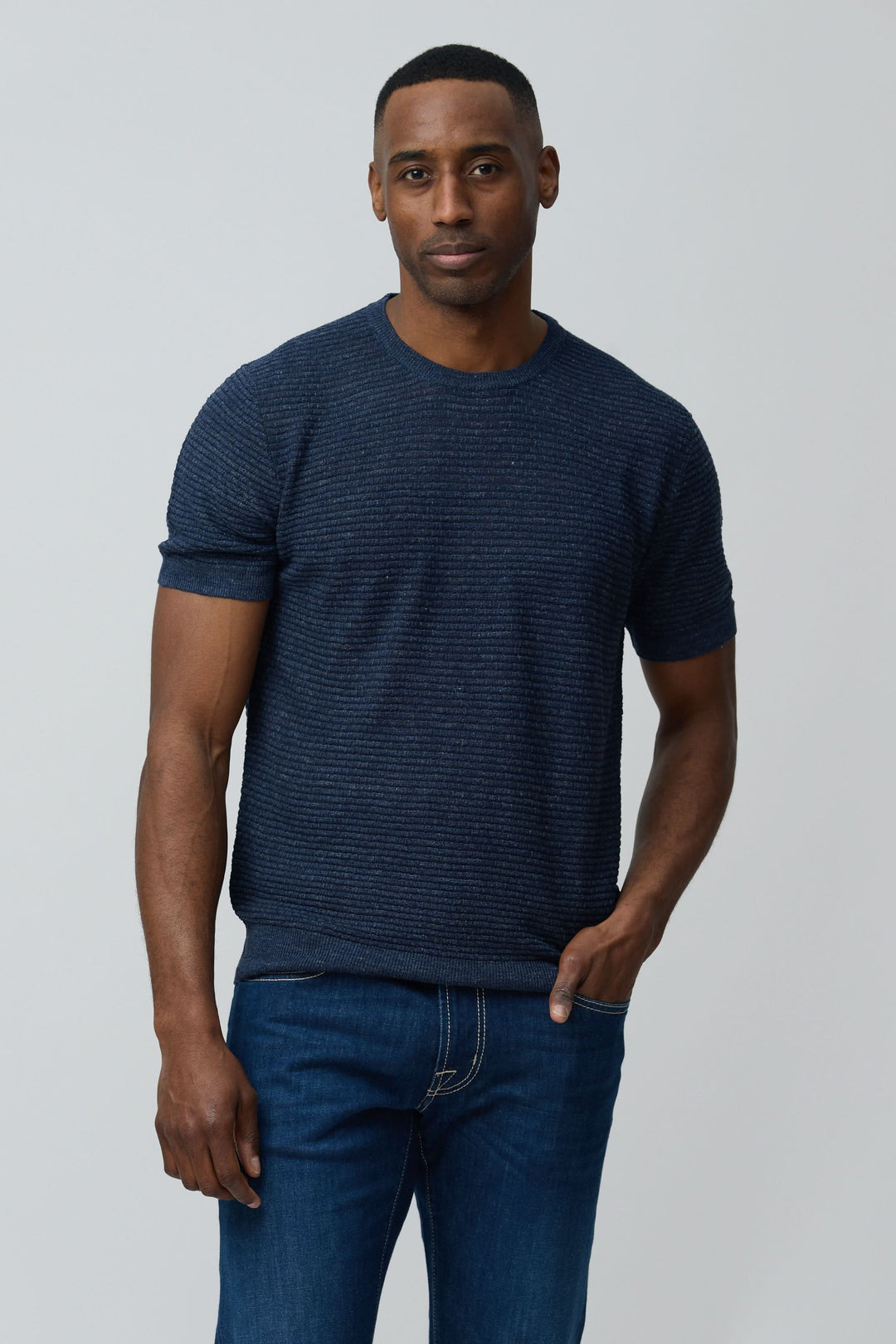 Homme portant un T-shirt texturé en lin et soie bleu, coupe ajustée avec manches courtes et col rond, style moderne et épuré.