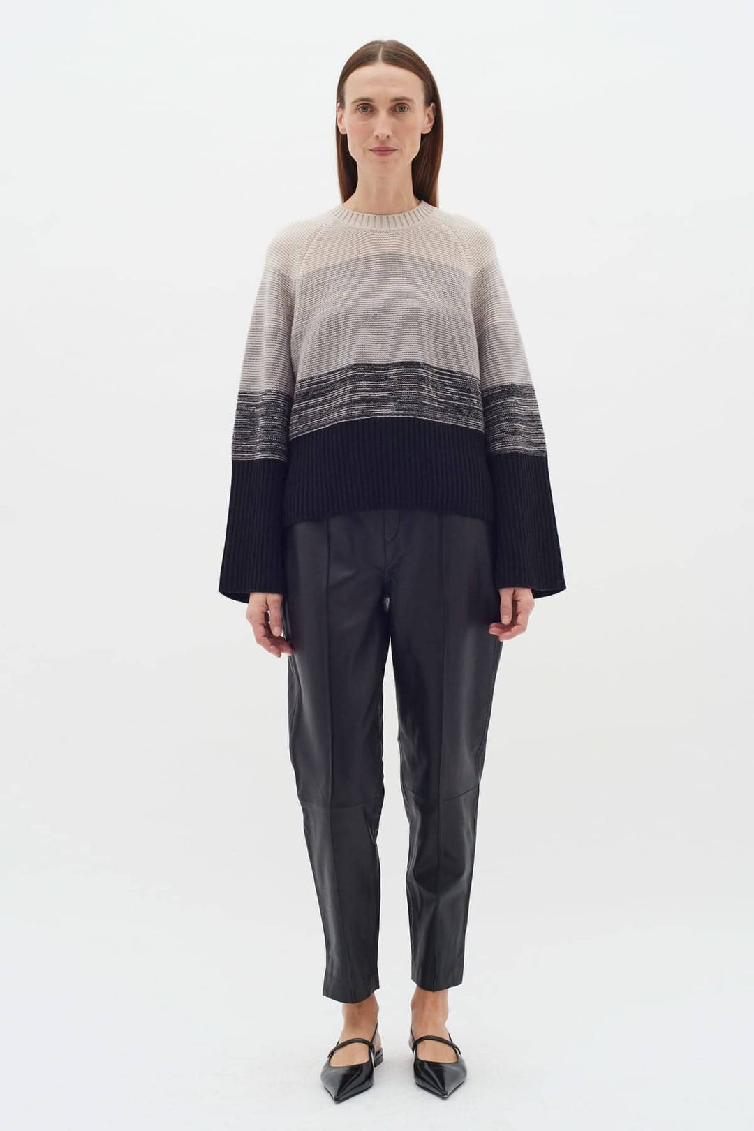 Femme portant un tricot Kaxy à rayures neutres, manches longues, associé à un pantalon en cuir noir.