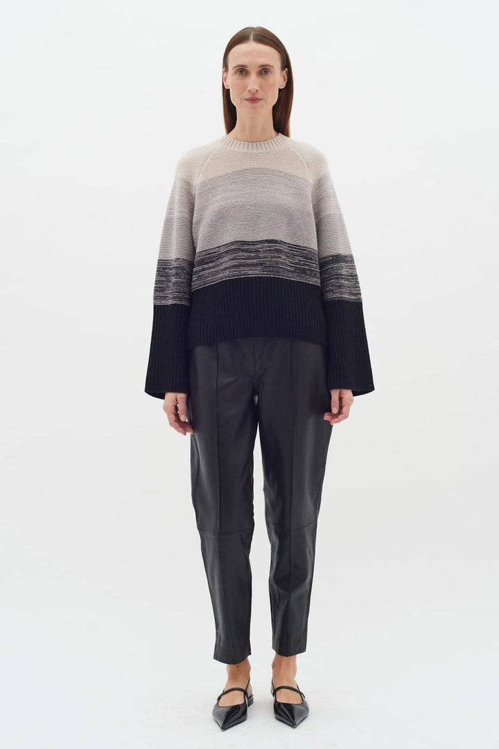 Femme portant un tricot Kaxy à rayures neutres, manches longues, associé à un pantalon en cuir noir.