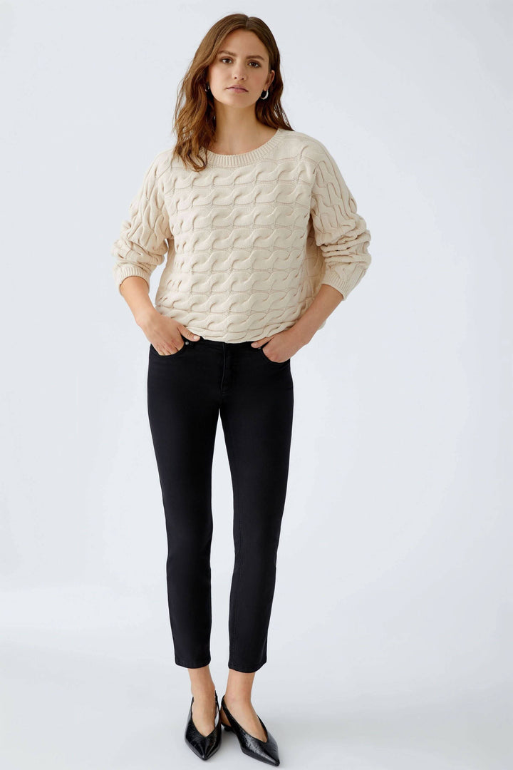 Modèle portant le Tricot Sirah à motif torsadé avec coupe carrée et col bateau élégant. Décris moi le produit en français.