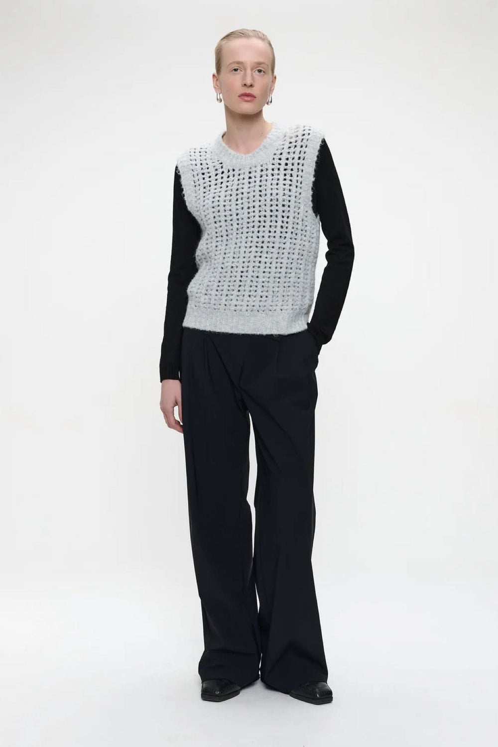 Tricot sans manches en maille ajourée porté sur un haut noir, style moderne et urbain chic