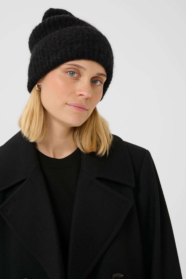 Femme portant la Tuque Sanja en tricot côtelé noir, style moderne et urbain, avec coupe allongée et revers ajustable.
