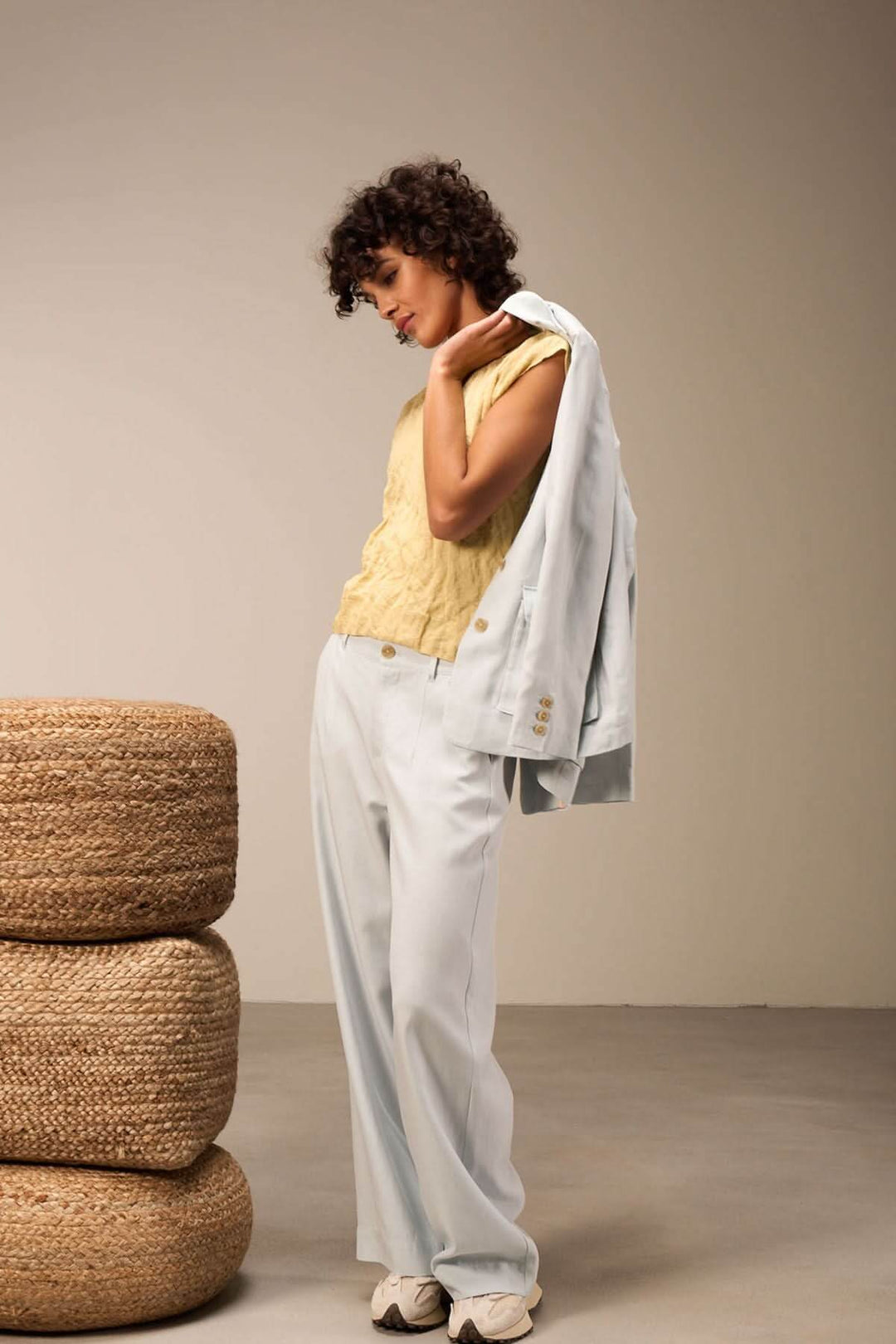 Femme en haut jaune et pantalon bleu clair, portant une veste sur l&