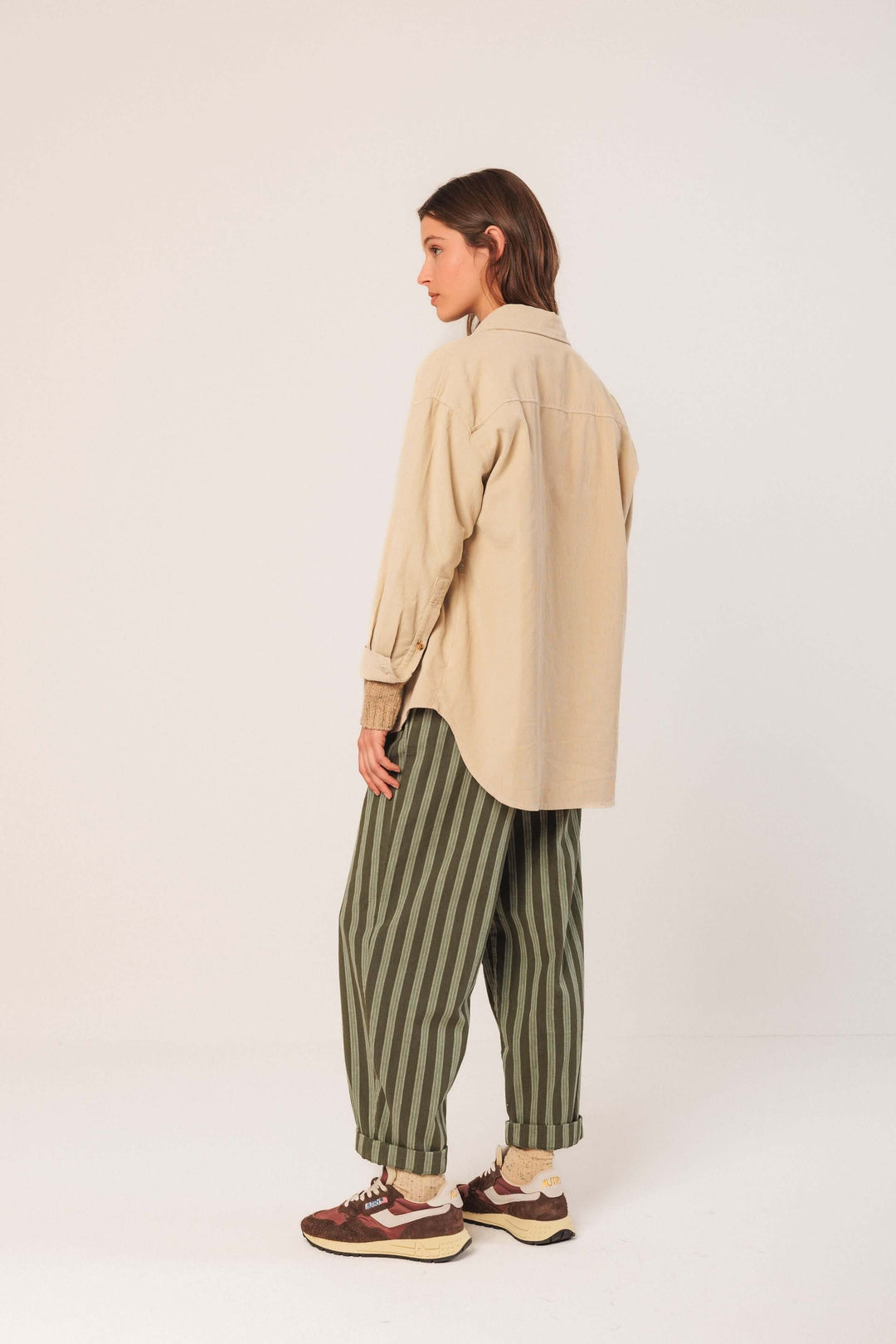 Femme portant une veste en velours côtelé beige avec pantalon rayé vert, vue de dos, style décontracté.