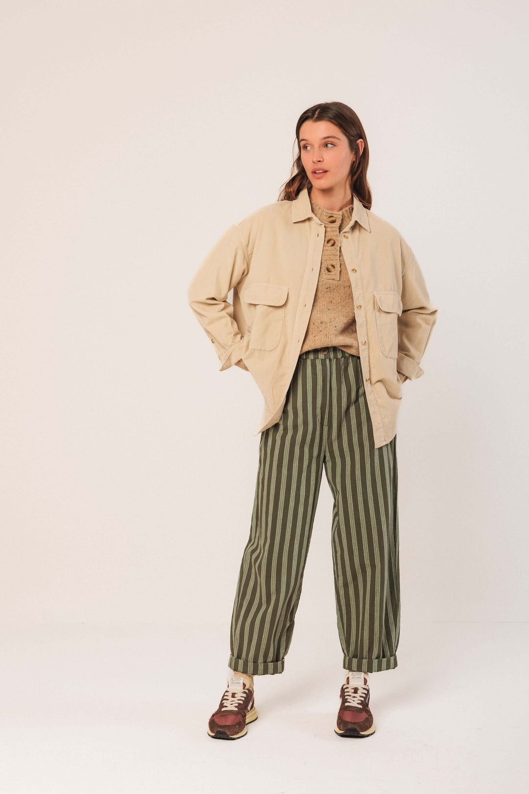 Femme portant une veste en velours côtelé beige avec un pantalon rayé vert large pour un look décontracté et tendance.